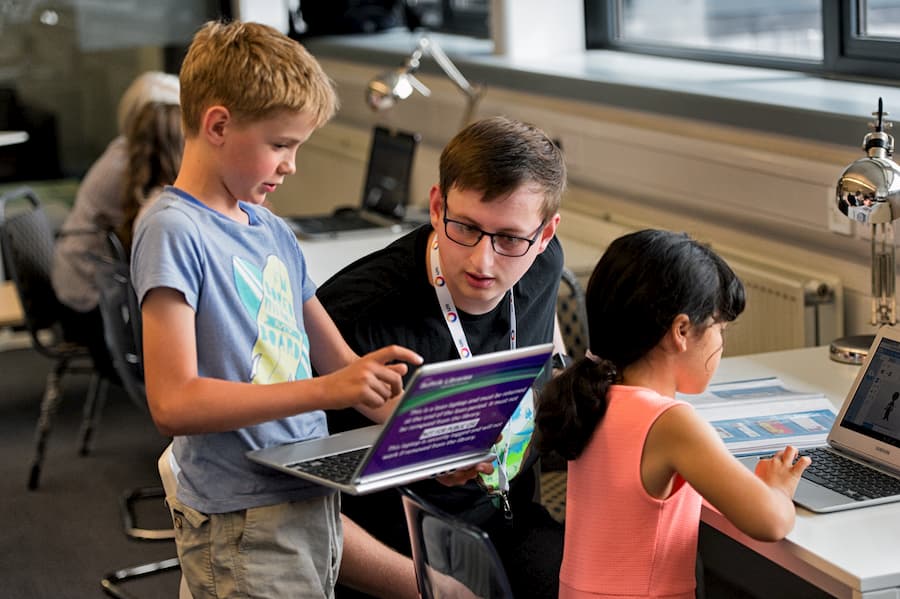 A young man helping children use laptops.