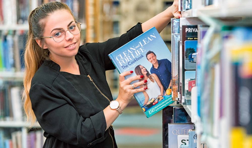 A woman placing a book on a library shelf.