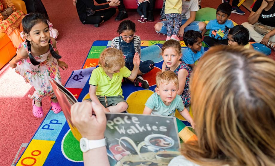 Woman reading to young children who are shouting and dancing.