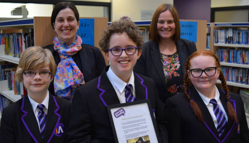 3 teachers and 2 pupils in a school library displaying a certificate