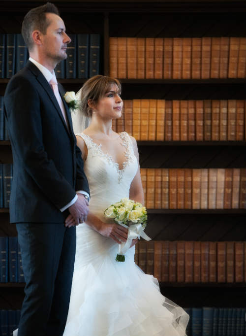 A wedding couple in front of a shelf of old, leather-bound books