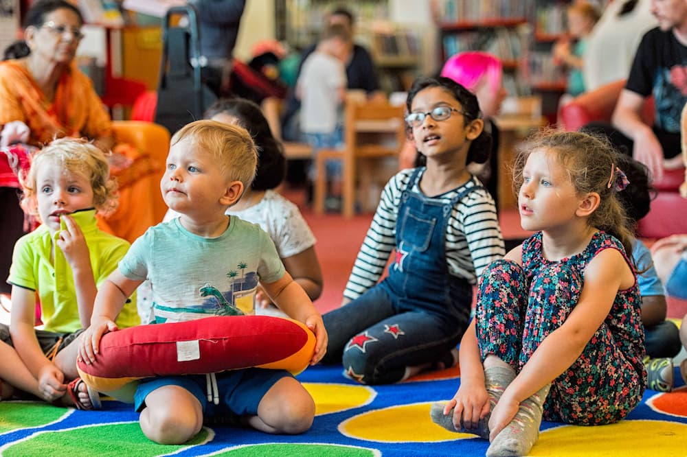 Children sat on a carpet in a library.