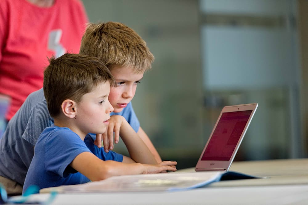 Two children concentrating at a laptop.