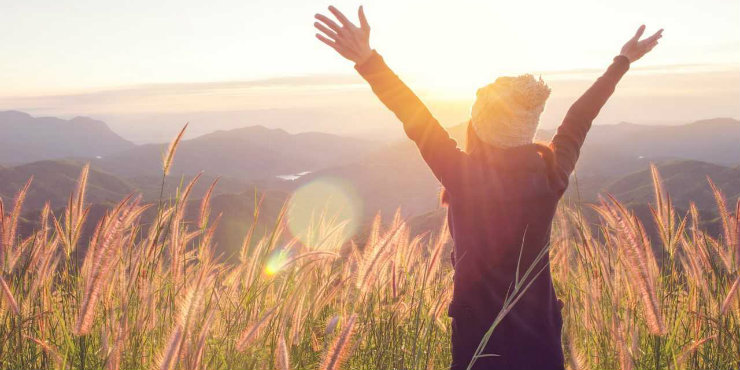 A woman in a field raising her arms to the sun