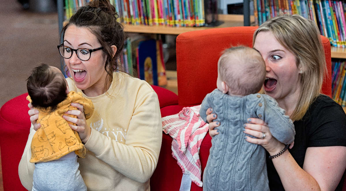 Two women playing with babies in a library.